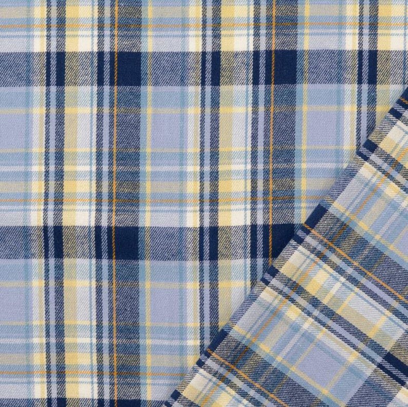 May include: Close-up of a fabric with a plaid pattern. The fabric features a combination of light blue, navy blue, yellow, and white colors. The plaid design is composed of intersecting vertical and horizontal lines, creating a grid-like pattern. The fabric is folded over on the right side.