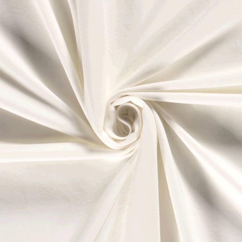 May include: White fabric with a smooth, silky texture. The fabric is draped and folded to create a swirling pattern.