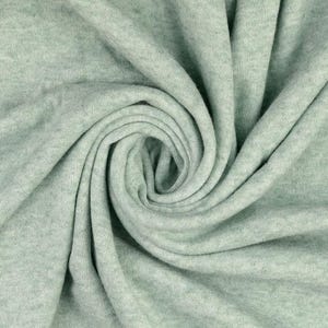 May include: Close-up of a soft, light green fabric with a swirling pattern. The fabric appears to be knit or woven, with a subtle texture and a muted, pastel color. The folds create shadows and depth.