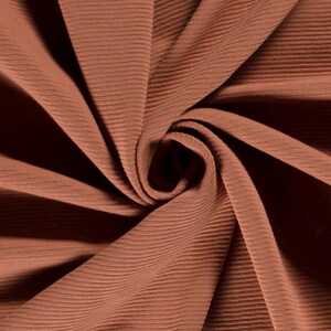 May include: Close-up of a rust-colored ribbed fabric. The fabric is soft and has a subtle texture.