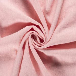 May include: Close-up of a swirl of soft, light pink fabric. The fabric has a textured appearance with visible folds and creases, creating a sense of depth and movement. The color is a delicate, muted pink.