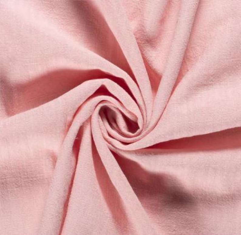 May include: Close-up of a swirl of soft, light pink fabric. The fabric has a textured appearance with visible folds and creases, creating a sense of depth and movement. The color is a delicate, muted pink.