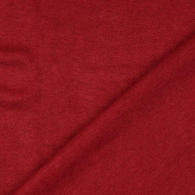 May include: Close-up of a solid red fabric with a subtle texture. The material is folded diagonally across the frame, creating a play of light and shadow. The fabric appears to be a medium weight, suitable for apparel or home decor.