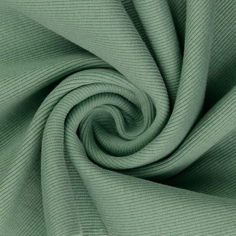 May include: Close-up of a sage green ribbed knit fabric. The fabric is tightly woven with vertical ridges, creating a textured surface. The fabric is folded and swirled, showing the depth and drape of the material. The color is a muted, earthy green.