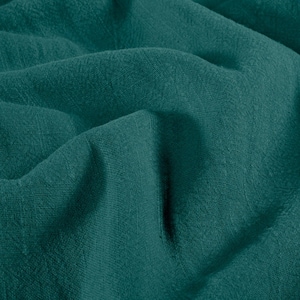 May include: Close-up of a teal-colored fabric with a textured weave. The fabric is draped, creating soft folds and shadows. The color is a deep, saturated teal, with subtle variations in tone across the surface. The material appears to be lightweight and breathable.