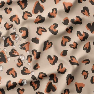 Könnte beinhalten: Ein beiger Stoff mit einem sich wiederholenden Muster aus braunen und orangefarbenen Leopardenflecken. Der Stoff hat einen leichten Glanz und Wassertropfen sind auf der Oberfläche sichtbar.