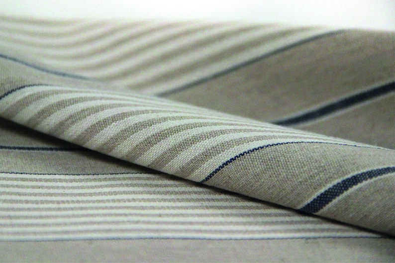 Pu&ograve; includere: Primo piano di un tessuto piegato con un motivo a righe in tonalit&agrave; beige e blu.