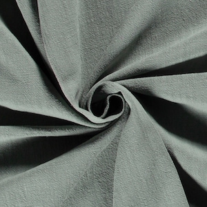 May include: Close-up of a swirl of sage green fabric. The fabric has a textured appearance with visible woven threads. The folds create shadows and highlights, emphasizing the material's softness and drape. The fabric is likely used for clothing or home decor.