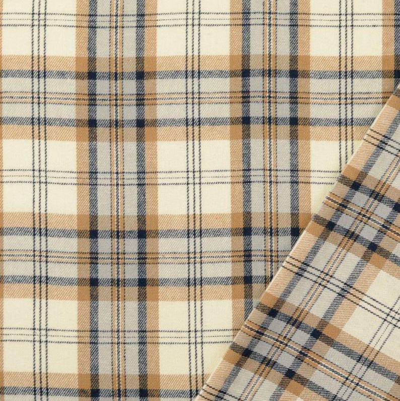 May include: Close-up of a plaid fabric with a cream-colored background and a grid pattern of tan and navy blue lines. A corner of the fabric is folded over, revealing the pattern on the reverse side. The fabric has a woven texture.