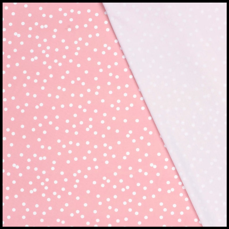 May include: Pink fabric with a white polka dot pattern. The fabric is folded in half, with the polka dot side facing up and the plain white side facing down.