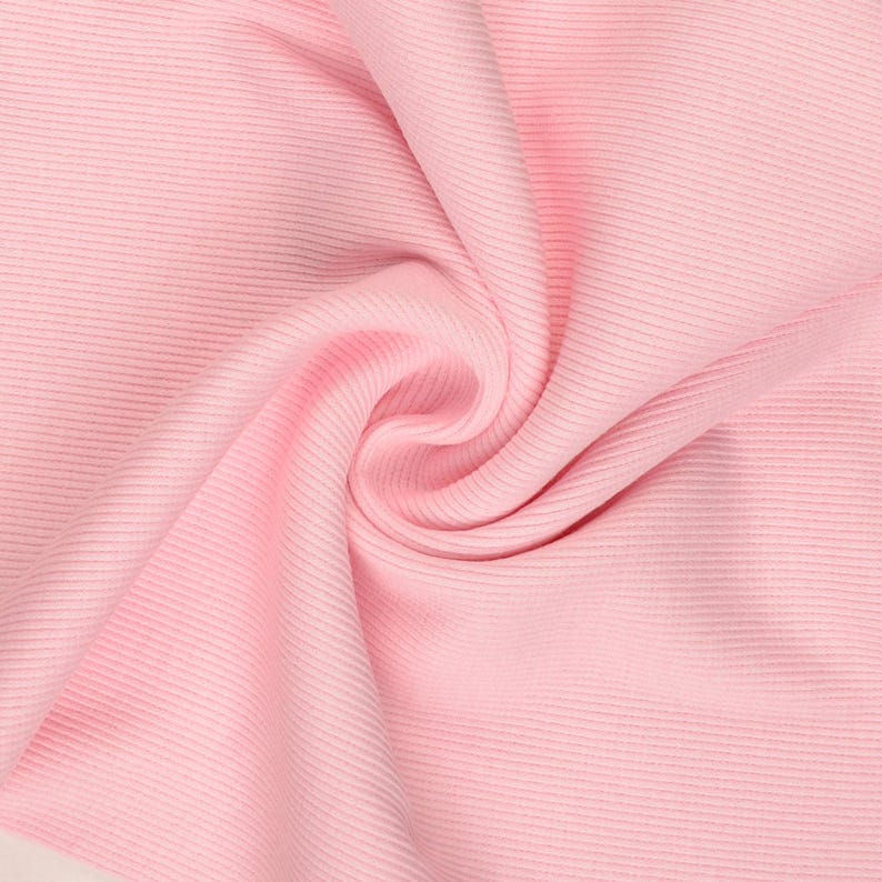 May include: Close-up of a soft, pink fabric with a ribbed texture. The fabric is gathered and folded, creating a swirling pattern. The color is a light, pastel pink, and the material appears to be smooth and flowing.
