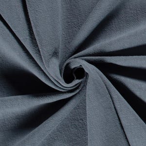 May include: Close-up of a swirl of textured, blue-grey fabric. The fabric has a soft, slightly wrinkled appearance, with shadows creating depth and dimension. The material is tightly woven, suggesting a durable textile.