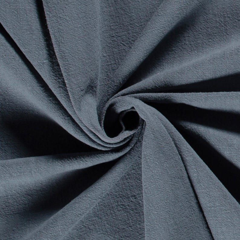 May include: Close-up of a swirl of textured, blue-grey fabric. The fabric has a soft, slightly wrinkled appearance, with shadows creating depth and dimension. The material is tightly woven, suggesting a durable textile.