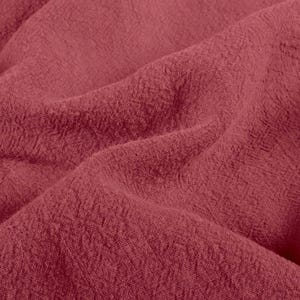 May include: Close-up of a textured, crumpled fabric in a deep rose color. The fabric has a slightly rough, woven appearance with visible folds and shadows, suggesting a soft, draping material. The overall effect is one of warmth and depth.