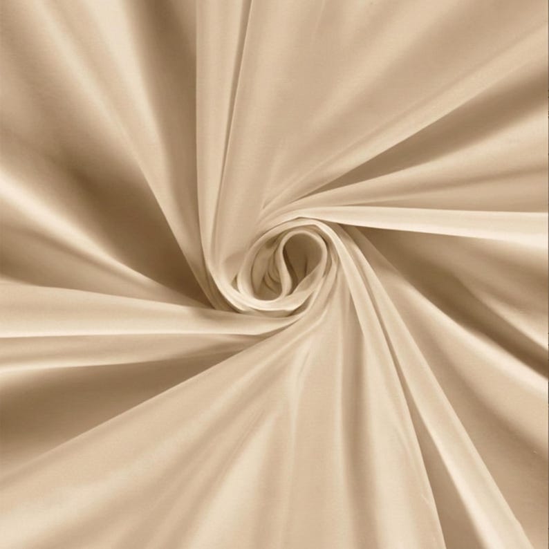 Pu&ograve; includere: Primo piano di un vortice di tessuto beige. Il tessuto ha una consistenza liscia e setosa con sottili riflessi e ombre. Le pieghe del tessuto creano un motivo a spirale, con il centro del vortice che appare pi&ugrave; chiaro.