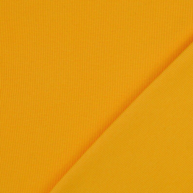 May include: Close-up of a vibrant, golden-yellow fabric with a ribbed texture. The fabric is folded diagonally, revealing a smooth, flat surface on the right side. The material appears to be a knit or woven textile, suitable for apparel or home decor.