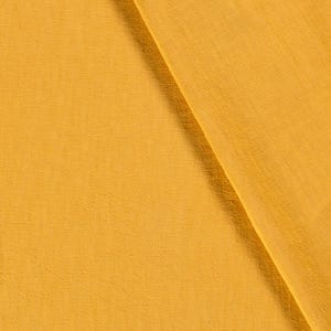 May include: Close-up of a folded piece of fabric in a warm, golden-yellow hue. The material has a subtle texture, with visible woven threads. The fabric is draped diagonally, creating a play of light and shadow.