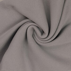 May include: Close-up of a gray ribbed fabric with a soft, flowing texture. The fabric is folded and draped, showcasing the horizontal ribbing pattern. The color is a muted, neutral gray, suitable for various apparel and textile projects.