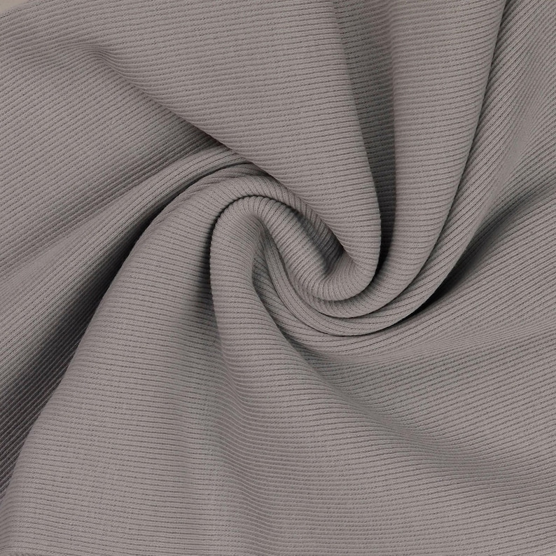 May include: Close-up of a gray ribbed fabric with a soft, flowing texture. The fabric is folded and draped, showcasing the horizontal ribbing pattern. The color is a muted, neutral gray, suitable for various apparel and textile projects.