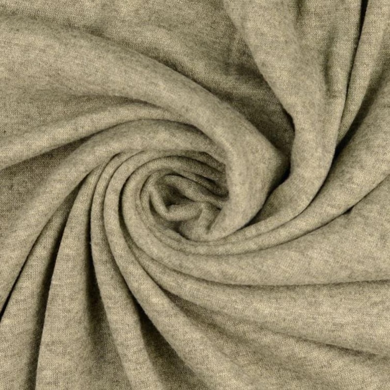 May include: Close-up of a swirl of soft, light gray fabric. The material is tightly woven, with visible texture and folds creating a dynamic pattern. The fabric appears to be a knit or jersey material, suitable for clothing.