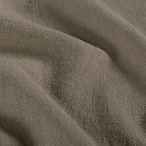 May include: Close-up of a textured, taupe-colored fabric. The material has a slightly wrinkled appearance, with visible woven threads and subtle variations in tone. The fabric drapes in soft folds, creating shadows and highlights.