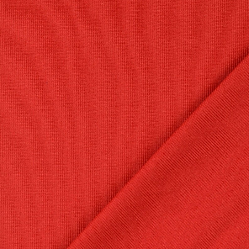 May include: A close-up of a vibrant red fabric with a ribbed texture. The fabric is folded diagonally, revealing the texture and color variations. The material appears to be a knit or similar textile.
