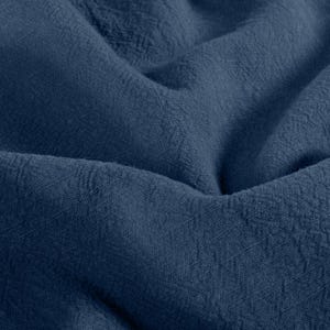May include: Close-up of a textured, navy blue fabric. The fabric is folded and draped, creating shadows and highlighting the woven texture. The deep blue color suggests a natural dye.