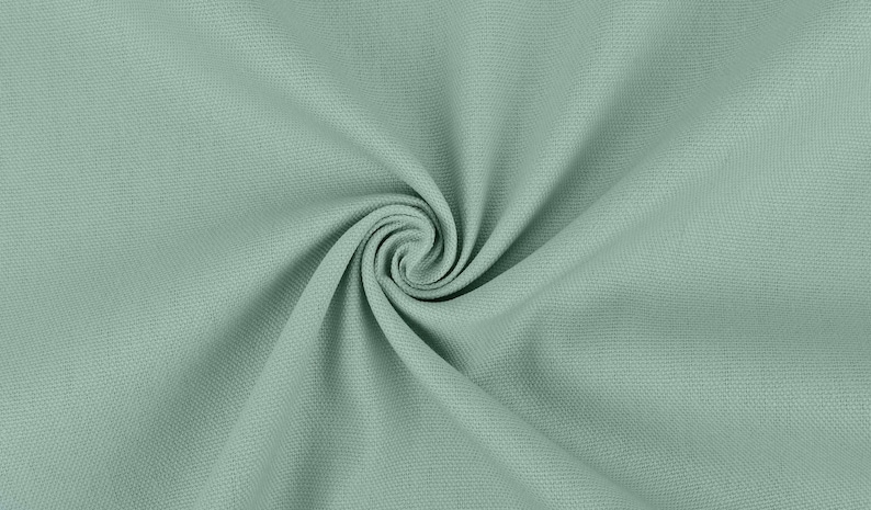May include: A close-up of a soft, light green fabric with a textured surface. The fabric is folded and twisted, creating a swirling pattern.