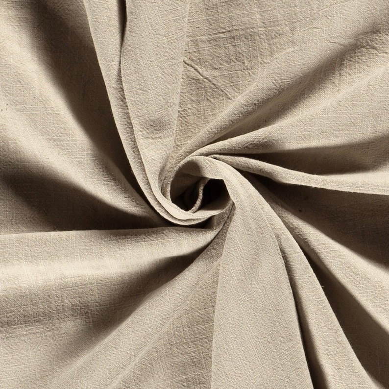 May include: Close-up of a beige fabric with a textured weave. The fabric is draped and swirled, creating a spiral effect in the center. The material appears soft and lightweight, with subtle variations in color.