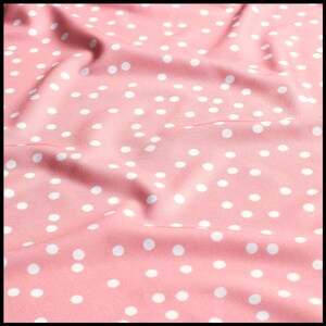 May include: Pink fabric with a white polka dot pattern. The fabric is wrinkled and has a soft, smooth texture.