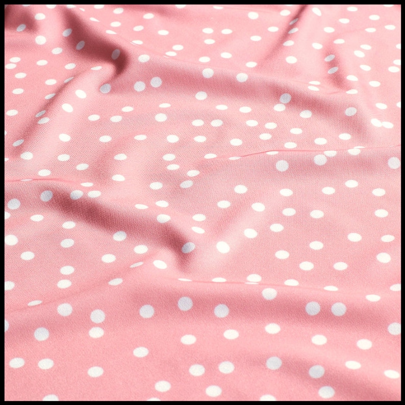 May include: Pink fabric with a white polka dot pattern. The fabric is wrinkled and has a soft, smooth texture.
