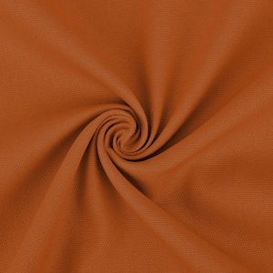 May include: Close-up of a rust-colored fabric with a textured surface. The fabric is folded and twisted, creating a swirling pattern.