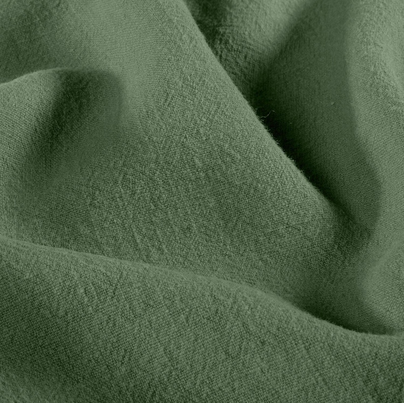 May include: Close-up of olive green fabric with a textured, woven appearance. The fabric is folded, creating shadows and highlighting the material's subtle variations in color and texture. The overall effect is soft and natural.