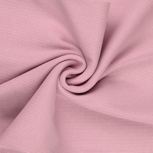 May include: Close-up of a swatch of pink ribbed fabric. The fabric is folded and draped, showing the texture and direction of the ribbing. The color is a soft, muted pink.