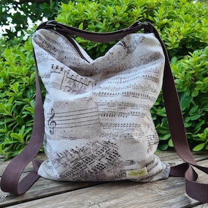 Puede incluir: Una bolsa de lona marrón con estampado de notas musicales. La bolsa tiene una correa ajustable marrón y una pequeña etiqueta verde con el texto "The Vintage" en ella.