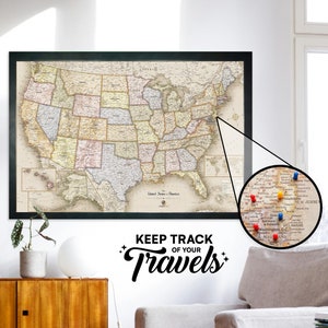 May include: A vintage-style map of the United States with push pins marking locations. The map is framed in black and hangs on a white wall. The text "Keep Track of Your Travels" is written below the map.