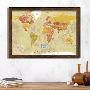 May include: A framed world map with a vintage aesthetic. The map is beige with brown and orange accents. The map is titled "Adventure Awaits" and features a compass rose. The frame is brown wood.