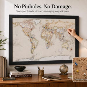 May include: A framed world map with a light beige background and black frame. The map features colourful magnetic pins placed on various countries. Text above the map reads: No Pinholes. No Damage. Track your travels with non-damaging magnetic pins.