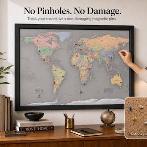 May include: A framed world map with a gray background and multicolored continents, featuring magnetic pins for tracking travel. The text reads: No Pinholes. No Damage. Track your travels with non-damaging magnetic pins. A small inset shows traditional push-pin maps.