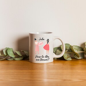 Puede incluir: Taza de cerámica blanca con una ilustración rosa y blanca de dos mujeres. El texto en la taza dice "Julie" y "Veux-tu être ma témoin?"