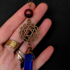 May include: A brass necklace with a star of David pendant, a blue lapis lazuli stone, and a red wooden bead with gold lettering.