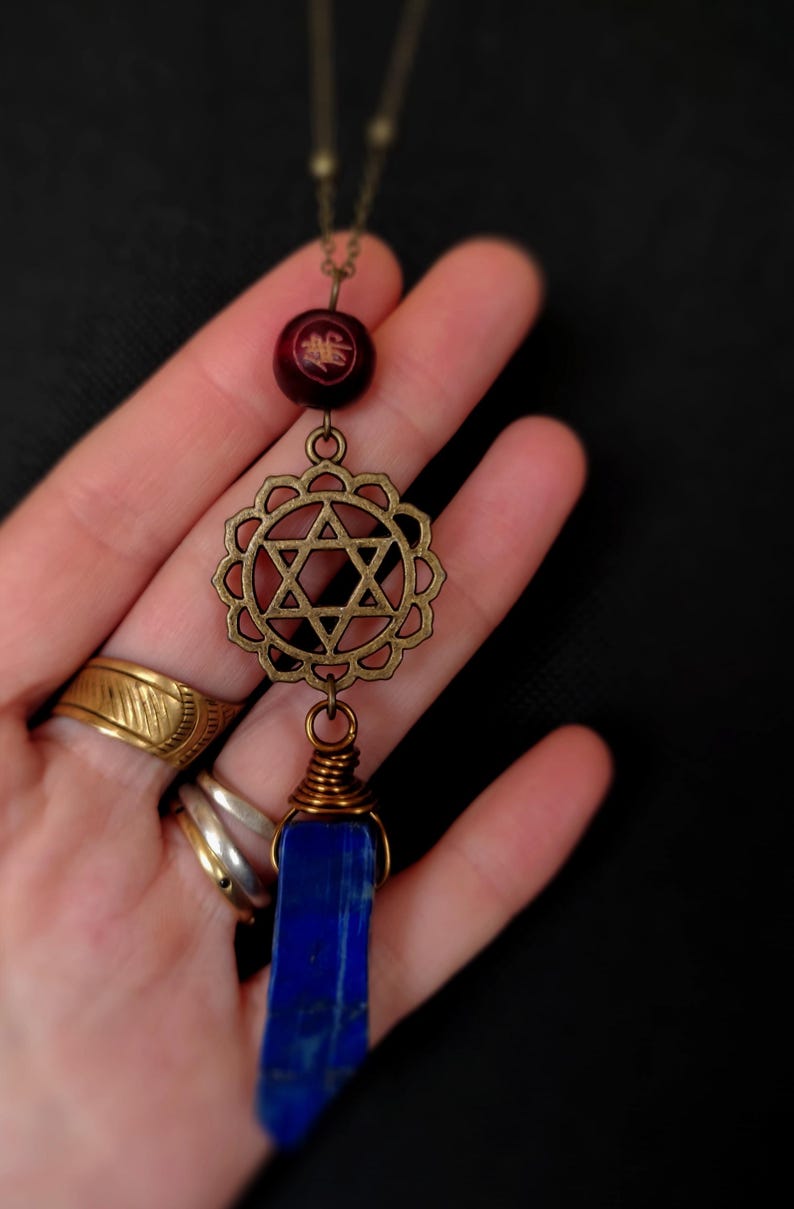 May include: A brass necklace with a star of David pendant, a blue lapis lazuli stone, and a red wooden bead with gold lettering.
