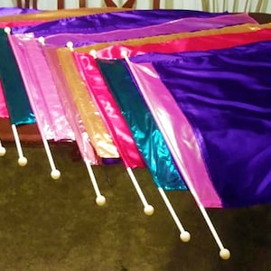 May include: A set of 10 colorful fabric flags with white poles. The flags are arranged in a row, with the longest flag at the top and the shortest flag at the bottom. The flags are made of a variety of materials, including satin, silk, and chiffon. The colors of the flags include purple, pink, red, orange, yellow, green, blue, and white.