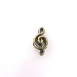 Könnte beinhalten: Ein bronzefarbener Notenschlüssel-Anhänger. Das Musiksymbol ist detailliert mit einem Wirbeldesign und einer kleinen Schlaufe zum Auffädeln. Der Anhänger ist vor einem weißen Hintergrund platziert.