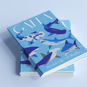 Può includere: Una pila di tre libri blu con un'illustrazione di squalo sulla copertina. Il libro in cima ha il titolo "GAIA" e il libro in fondo ha il titolo "Secret Life Of Sharks".