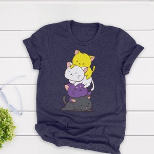 May include: Navy blue t-shirt with a cartoon cat design. The design features a stack of cats in yellow, white, purple, and grey. The cats are stacked on top of each other. The t-shirt has a crew neck and short sleeves.