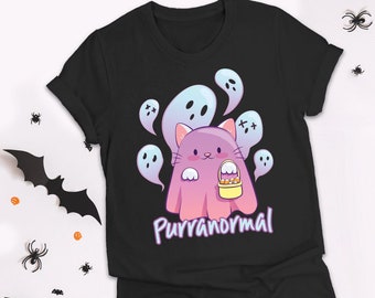 May include: Black t-shirt featuring a cartoon cat dressed as a ghost, holding a basket of candy. The cat is pink and surrounded by blue ghosts. The text "Purranormal" is below the cat in a purple font. Halloween theme.