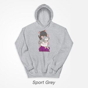 Puede incluir: Una sudadera con capucha gris con una pila de cuatro gatos de dibujos animados en la parte delantera. Los gatos est&aacute;n apilados uno encima del otro, con el gato de abajo morado, el siguiente blanco, el siguiente gris y el gato de arriba negro. Todos los gatos tienen la nariz rosa y bigotes.