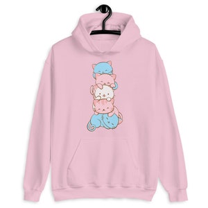 May include: Pink hoodie with a stack of four cartoon cats in different colors. The cats are stacked on top of each other, with the smallest cat on the bottom and the largest cat on top. The cats are all looking at the viewer.