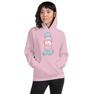 May include: A pink hoodie with a stack of four cartoon cats in different colors. The cats are stacked on top of each other, with the bottom cat being blue, the next cat being pink, the next cat being white, and the top cat being blue.